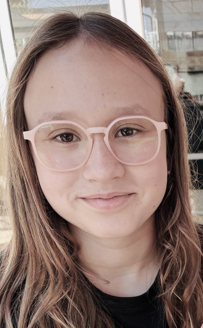 Lächelndes Mädchen mit langen, braunen Haaren und rosa Brille.
